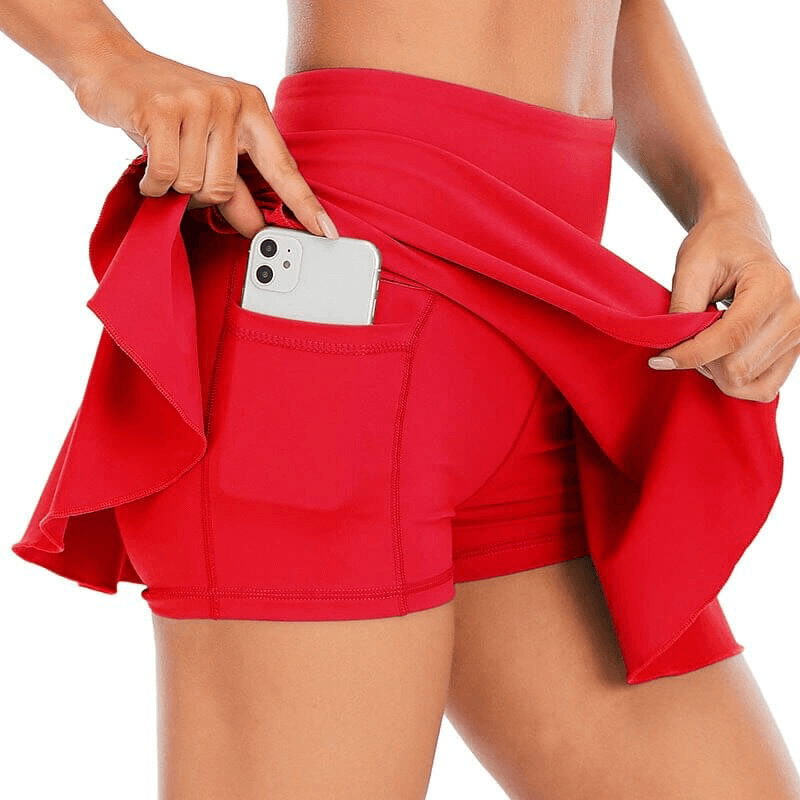 Woman in red high waist skirt-shorts for tennis, featuring a convenient pocket for a phone, showcasing comfort and practicality.